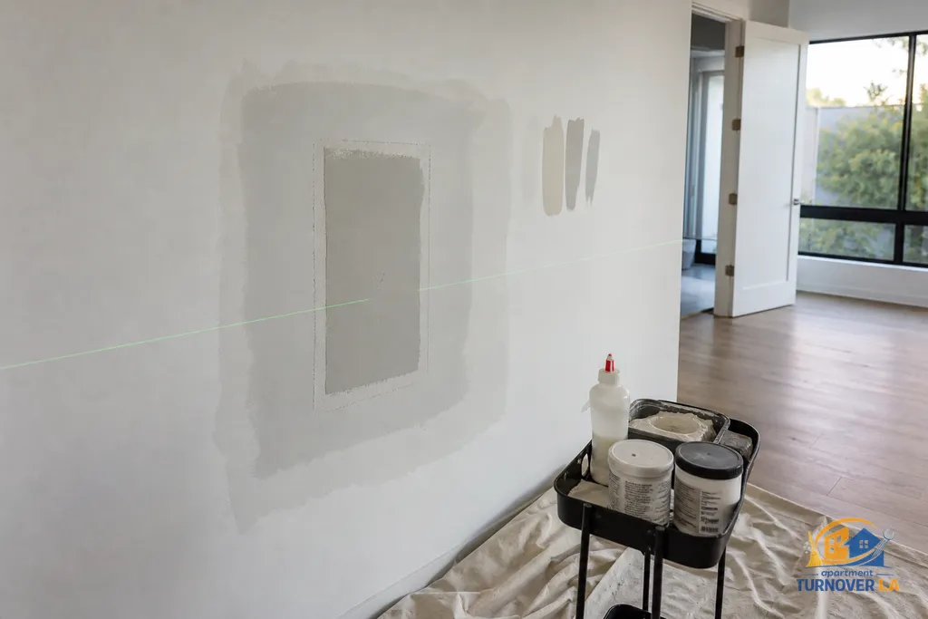 Medium drywall repair around old TV mount with mesh tape and feathered compound in a West Hollywood bedroom, texture bottle and paint samples visible