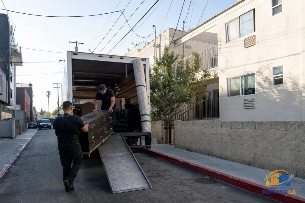 Crew loads an unwanted dresser into a box truck from a Koreatown alley, red curb and permit parking signs visible during a furniture removal