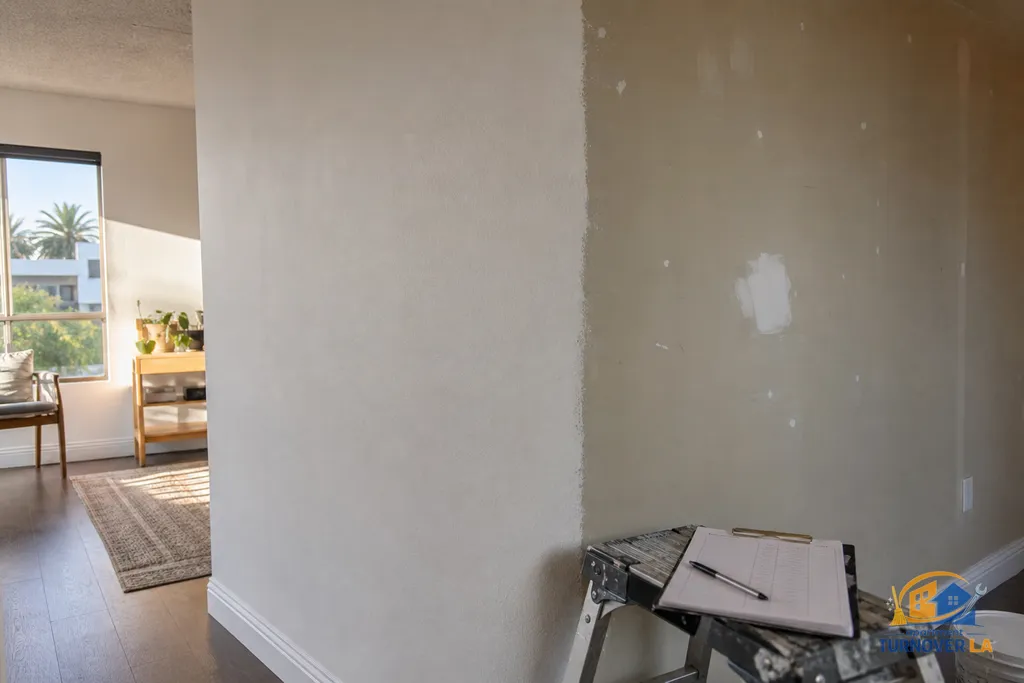 Living room corner with fresh eggshell finish beside patched nail holes and textured drywall repair, baseboards taped and ready