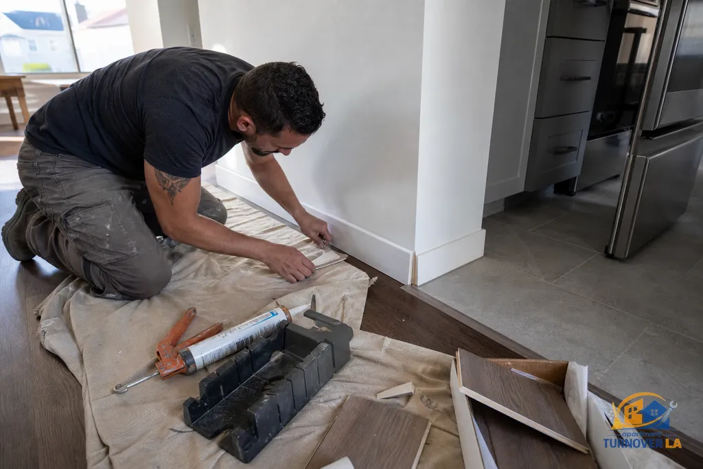 Handyman resetting baseboard and quarter round at the edge of new vinyl plank and kitchen tile in an LA rental