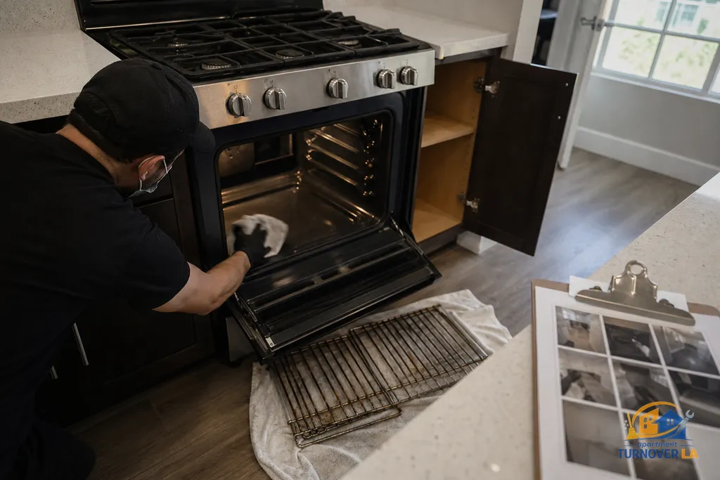 LA apartment kitchen mid deep clean, oven racks out and interior being wiped, cabinets open with a photo checklist on the counter