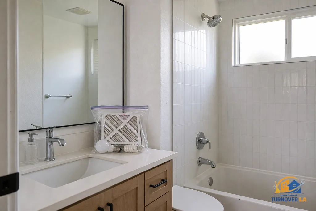 Detailed bathroom move-out clean in LA with scrubbed grout, descaled fixtures, dusted vent, and photo log items bagged on the vanity