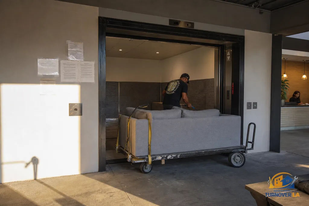 Downtown LA freight elevator loading bay with a couch on a dolly and posted building rules, showing high-rise furniture removal logistics